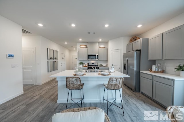 kitchen featuring hardwood / wood-style flooring, appliances with stainless steel finishes, a center island with sink, and gray cabinetry