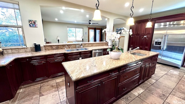 kitchen featuring stainless steel appliances, light stone counters, sink, a kitchen island with sink, and pendant lighting