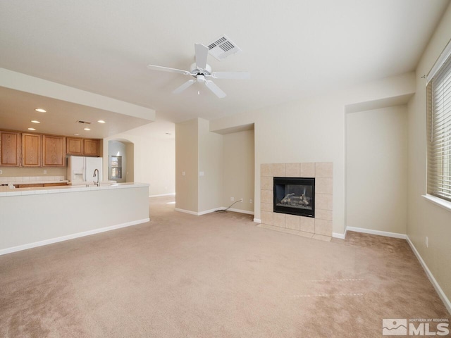 unfurnished living room featuring a tiled fireplace, light colored carpet, and ceiling fan