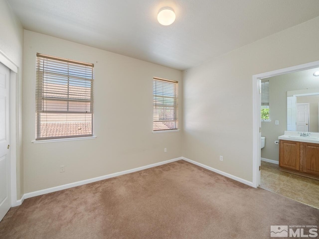 unfurnished bedroom featuring ensuite bathroom, light carpet, and sink