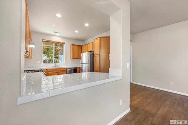 kitchen with stainless steel appliances, sink, tile counters, dark wood-type flooring, and kitchen peninsula