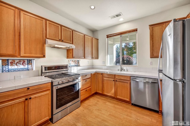 kitchen featuring tile counters, light wood-type flooring, stainless steel appliances, and sink