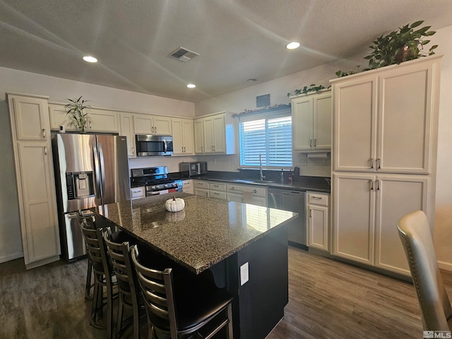 kitchen with appliances with stainless steel finishes, a textured ceiling, dark hardwood / wood-style flooring, dark stone countertops, and a center island