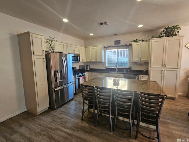 kitchen featuring a kitchen bar, a center island, a textured ceiling, dark hardwood / wood-style floors, and appliances with stainless steel finishes