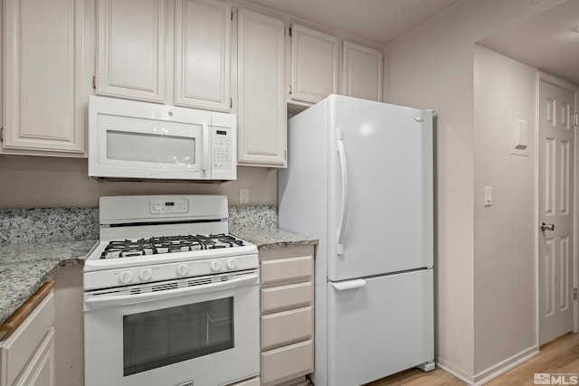 kitchen with white cabinetry, white appliances, light stone countertops, and light hardwood / wood-style floors