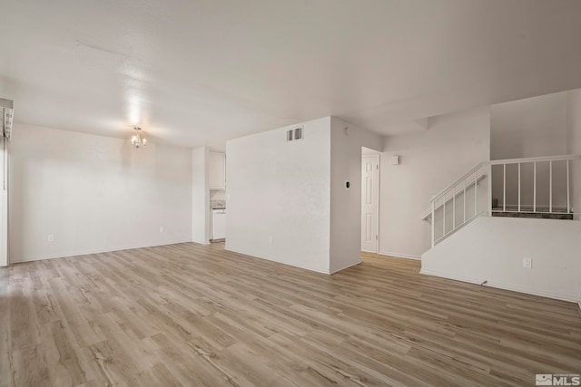 unfurnished living room with light wood-type flooring and a chandelier