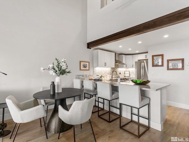 dining space featuring light hardwood / wood-style floors, beam ceiling, and sink