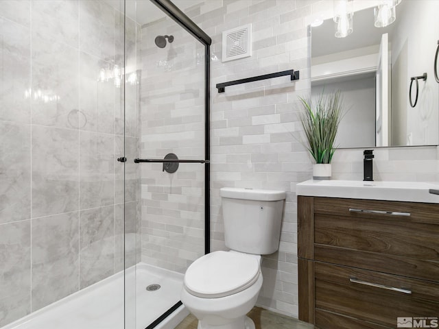 bathroom with tile walls, vanity, toilet, and a shower with shower door