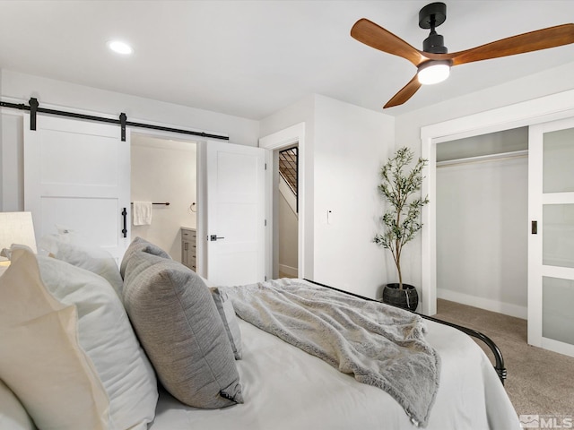 carpeted bedroom featuring a barn door, ensuite bathroom, ceiling fan, and a closet