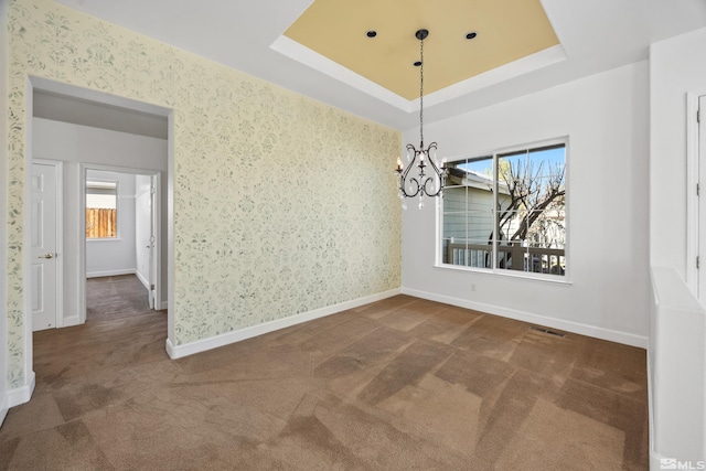 unfurnished dining area featuring dark colored carpet, an inviting chandelier, and a tray ceiling