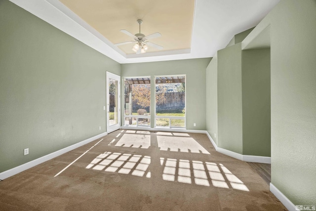 carpeted empty room with ceiling fan and a raised ceiling