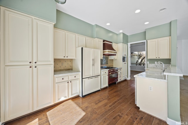 kitchen with high end stove, white refrigerator, custom range hood, dark wood-type flooring, and kitchen peninsula