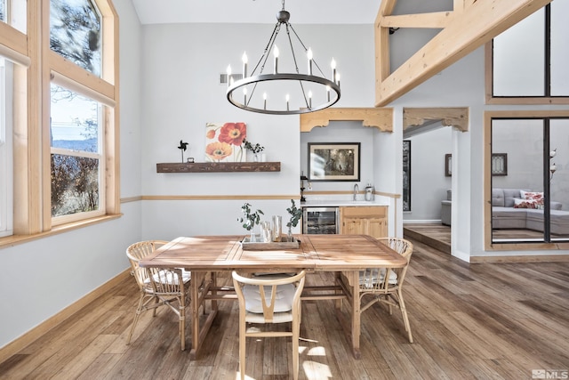 dining area featuring a towering ceiling, hardwood / wood-style floors, a chandelier, and wine cooler