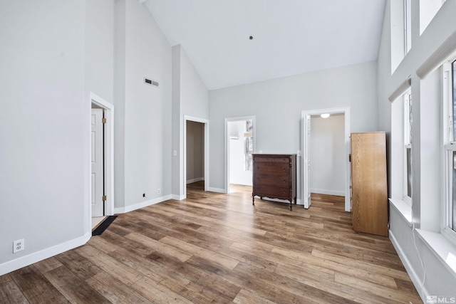 unfurnished bedroom with high vaulted ceiling, ensuite bath, wood-type flooring, and multiple windows