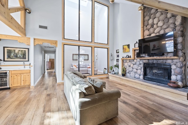 living room with wine cooler, sink, a fireplace, a towering ceiling, and light hardwood / wood-style flooring