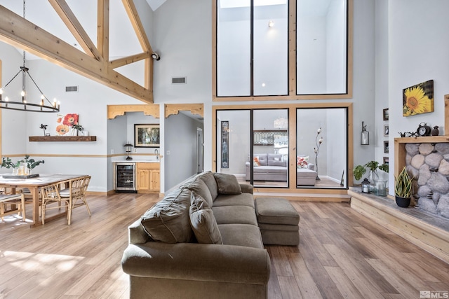 living room featuring sink, an inviting chandelier, high vaulted ceiling, wood-type flooring, and beverage cooler