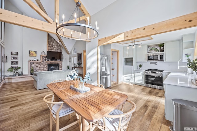 dining space featuring a fireplace, beam ceiling, high vaulted ceiling, sink, and light hardwood / wood-style floors