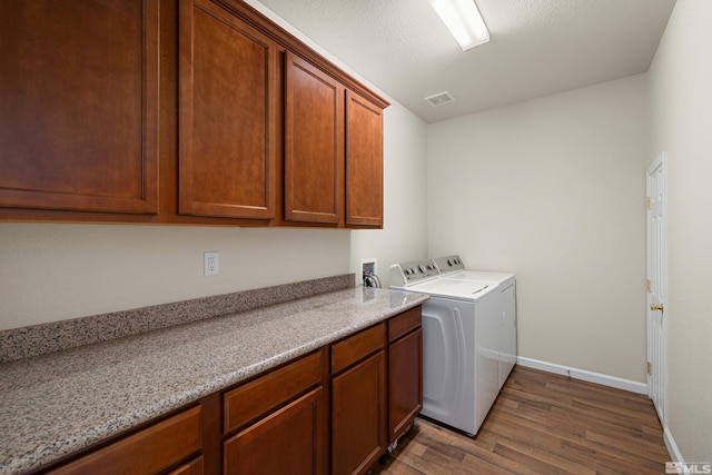 washroom with a textured ceiling, hardwood / wood-style floors, cabinets, and washer and dryer