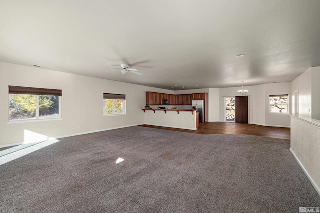 unfurnished living room featuring ceiling fan with notable chandelier, dark hardwood / wood-style flooring, and a healthy amount of sunlight