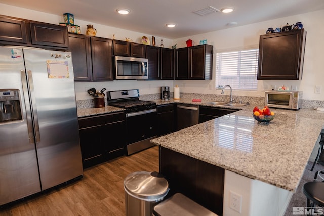 kitchen with dark brown cabinetry, light hardwood / wood-style floors, sink, appliances with stainless steel finishes, and a kitchen breakfast bar