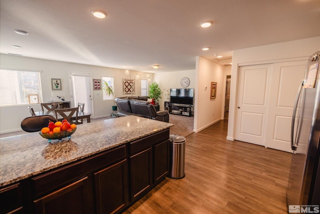 kitchen with dark brown cabinets, stainless steel refrigerator, light stone countertops, and light wood-type flooring