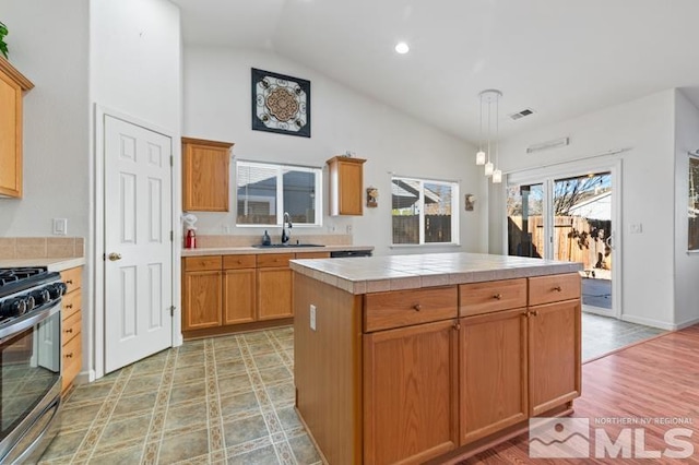 kitchen featuring hanging light fixtures, sink, stainless steel range with gas stovetop, lofted ceiling, and a center island