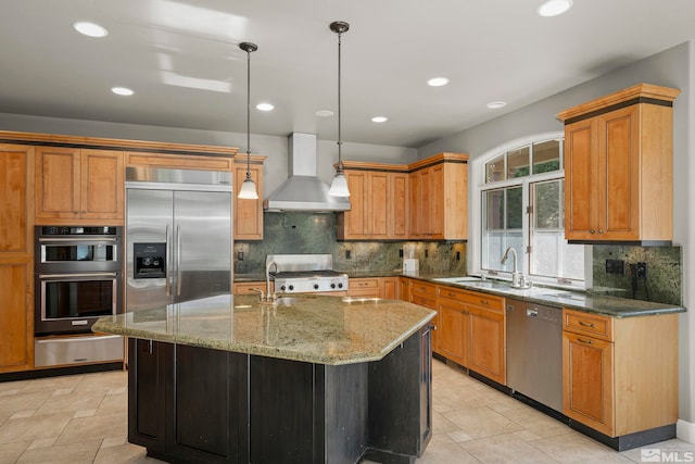 kitchen featuring stainless steel appliances, a center island with sink, backsplash, hanging light fixtures, and wall chimney range hood