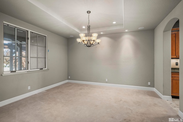 carpeted spare room with a tray ceiling and an inviting chandelier