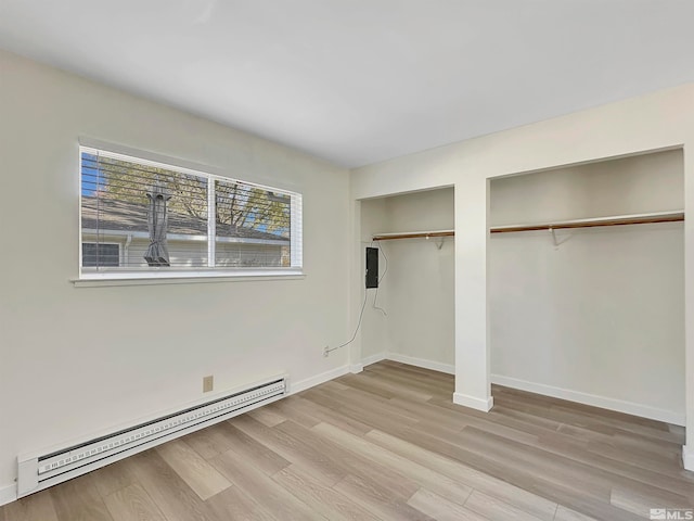 unfurnished bedroom with multiple closets, light wood-type flooring, and baseboard heating