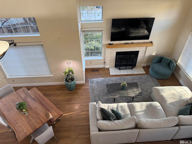 living room featuring a towering ceiling, a tiled fireplace, and hardwood / wood-style flooring