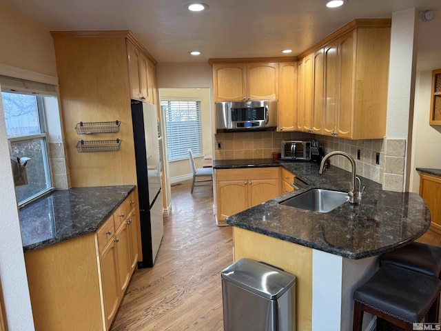 kitchen with dark stone counters, light wood-type flooring, white refrigerator, and sink