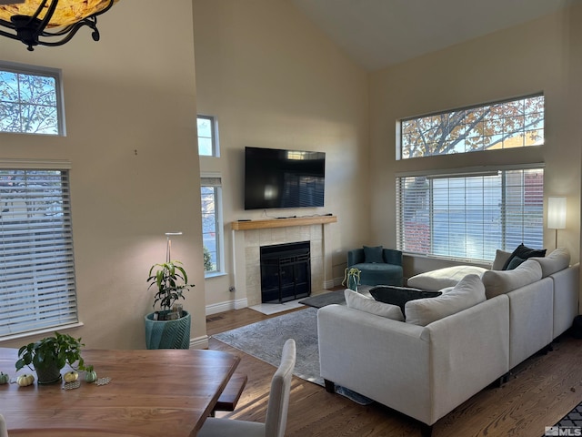 living room featuring a towering ceiling, a tiled fireplace, and hardwood / wood-style floors