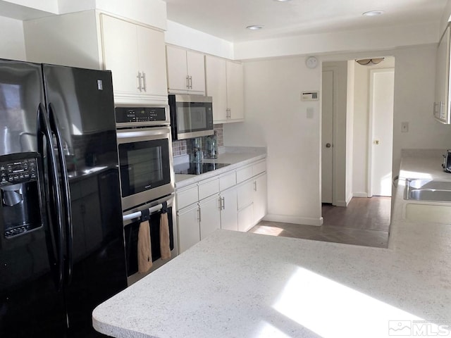 kitchen featuring backsplash, sink, black appliances, hardwood / wood-style flooring, and white cabinetry