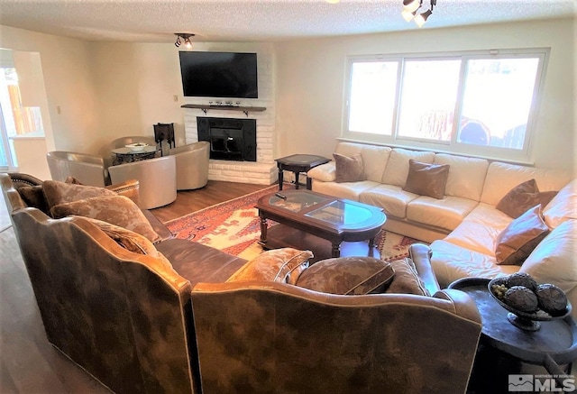 living room with hardwood / wood-style floors, a textured ceiling, and a brick fireplace