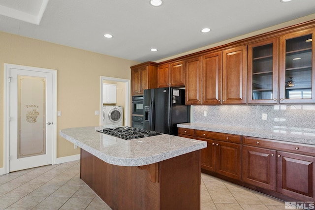 kitchen featuring black appliances, light tile patterned flooring, washer / dryer, backsplash, and a breakfast bar