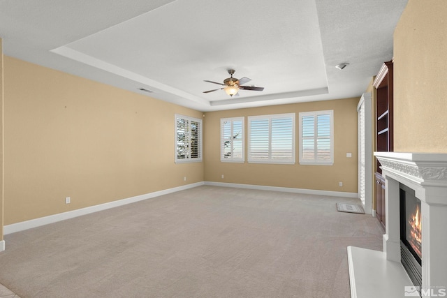 unfurnished living room featuring a textured ceiling, light carpet, ceiling fan, and a tray ceiling