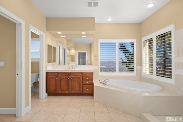 bathroom with tile patterned flooring, vanity, tiled tub, and toilet