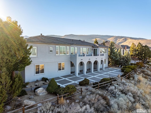 back of property with a balcony, a mountain view, and a patio area