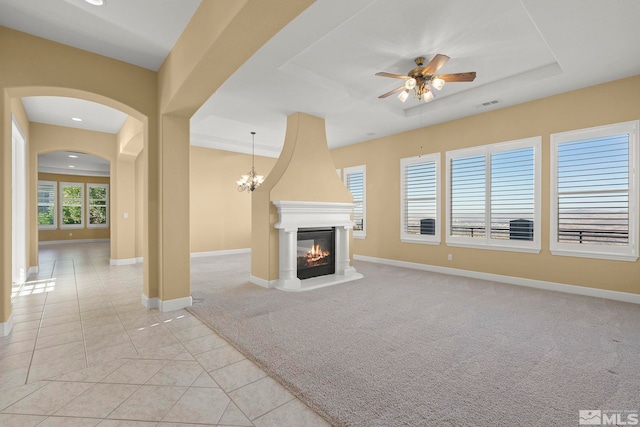 unfurnished living room featuring a raised ceiling, ceiling fan with notable chandelier, light carpet, and a fireplace