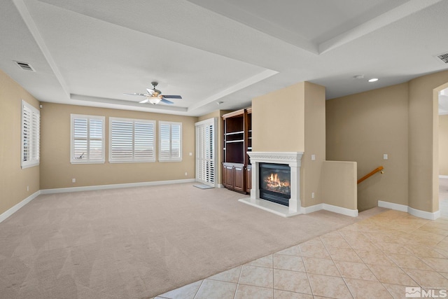 unfurnished living room with ceiling fan, light carpet, and a tray ceiling