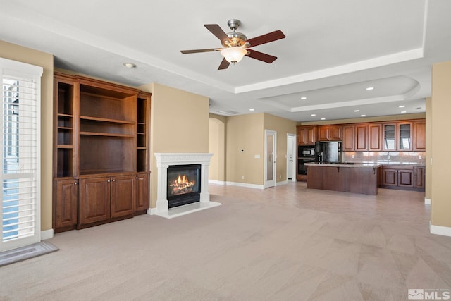 unfurnished living room with a tray ceiling, light colored carpet, and plenty of natural light