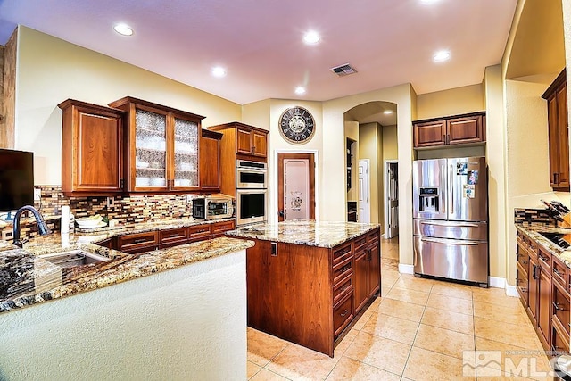 kitchen featuring stainless steel appliances, sink, light stone countertops, a center island, and decorative backsplash