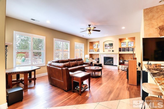 living room featuring light hardwood / wood-style flooring, ceiling fan, and a tile fireplace