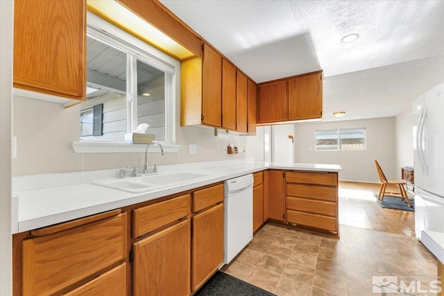 kitchen featuring kitchen peninsula, light wood-type flooring, a textured ceiling, white appliances, and sink