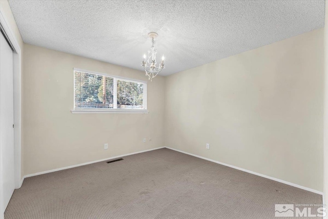 carpeted empty room featuring a notable chandelier and a textured ceiling