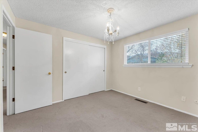 unfurnished bedroom with carpet flooring, a textured ceiling, a closet, and a notable chandelier