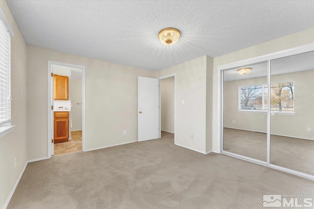 unfurnished bedroom with light carpet, a textured ceiling, a closet, and connected bathroom