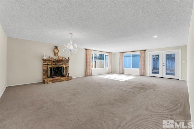 unfurnished living room with carpet floors, a fireplace, a textured ceiling, french doors, and a chandelier