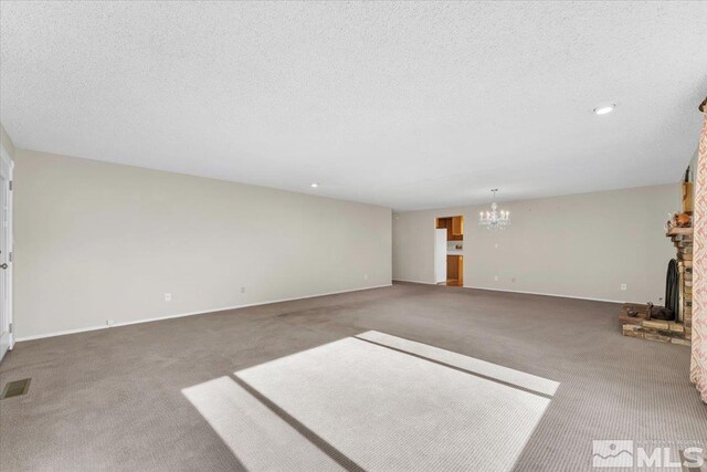 unfurnished living room with a fireplace, a textured ceiling, carpet floors, and a chandelier