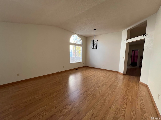 spare room with a textured ceiling, vaulted ceiling, and light hardwood / wood-style flooring